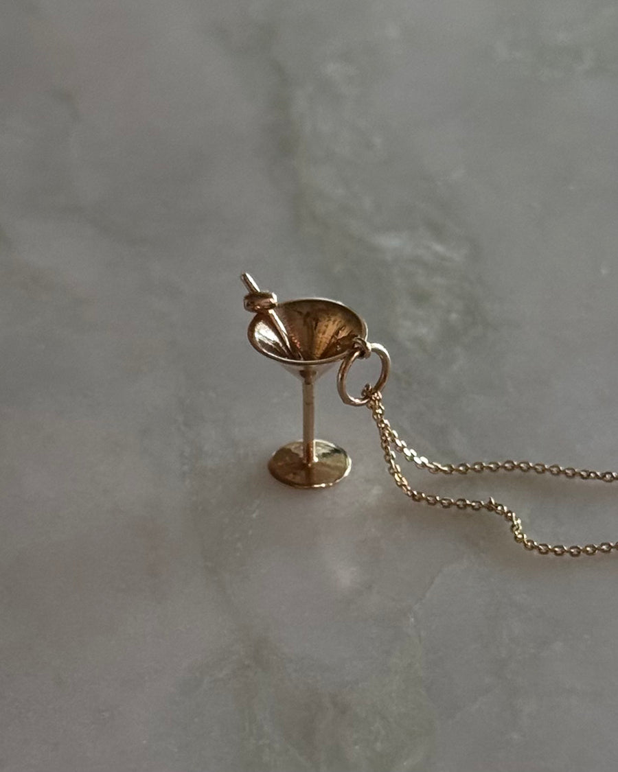 Gold necklace with a martini glass pendant on a gray background